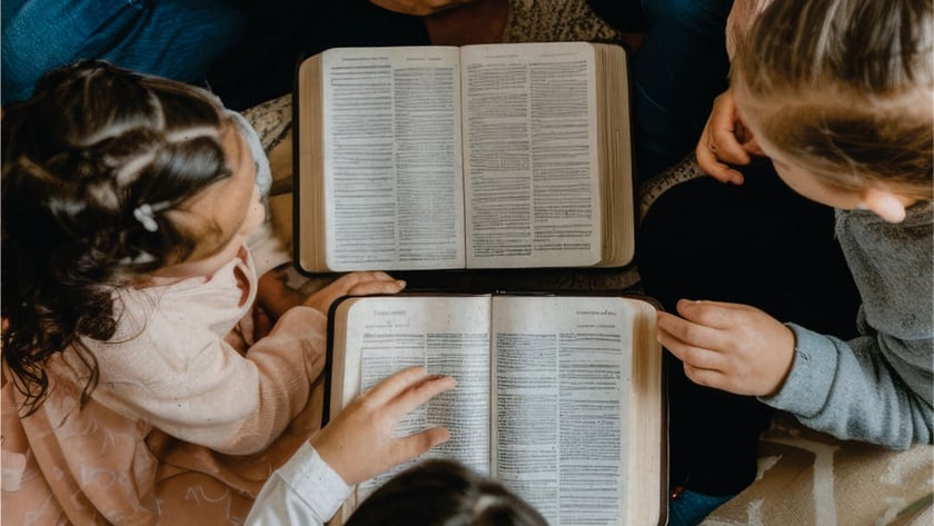 Crianças e adultos sentados em círculo no chão, lendo duas Bíblias abertas.