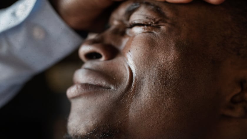 Homem de olhos fechados, com a mão na testa e lágrimas no rosto.