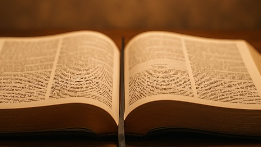 Livro grande aberto, com duas páginas de texto e uma fita marcadora, sobre mesa de madeira.