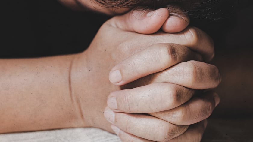 Pessoa de cabeça baixa, com as mãos entrelaçadas sobre uma Bíblia aberta.