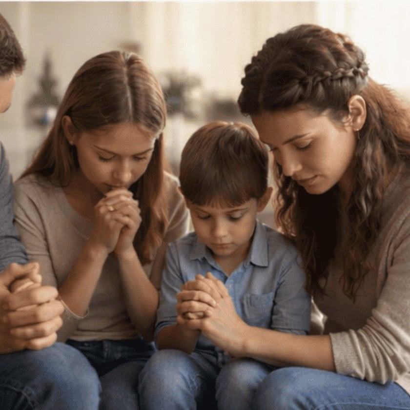 Mulher, menina e menino sentados juntos, de olhos fechados e mãos unidas, rezando.