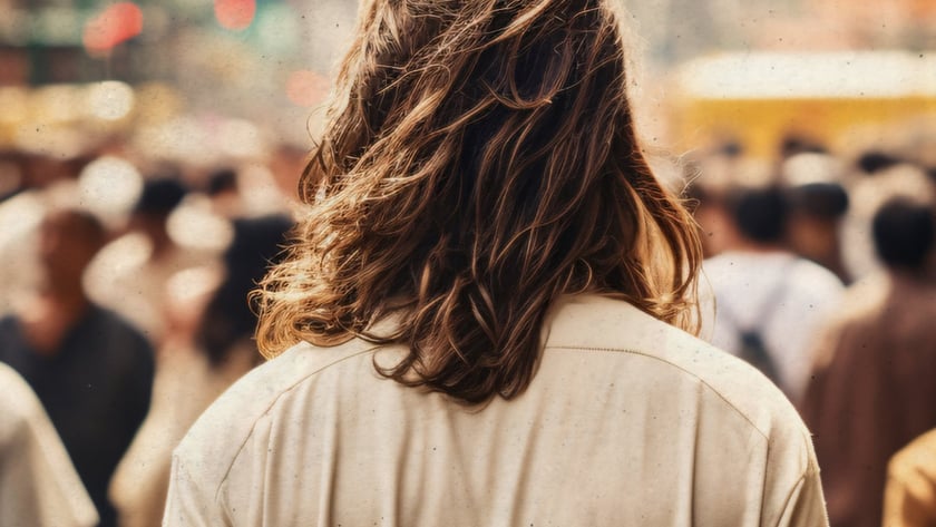 Pessoa de costas, com cabelo castanho ondulado e camisa clara, em meio a uma multidão