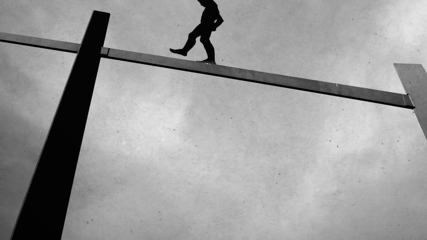 Silhueta de uma pessoa andando sobre uma viga de metal alta contra o céu nublado.