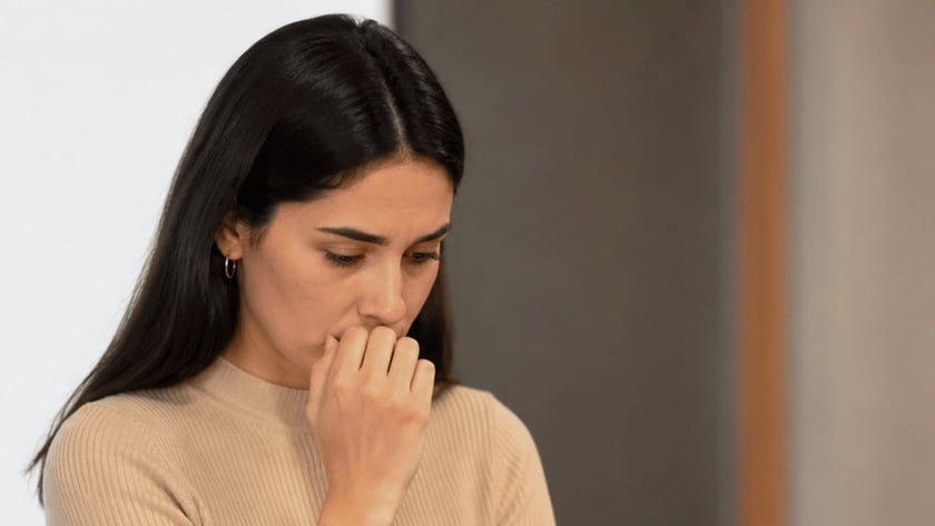 Mulher de cabelo escuro, com a mão na boca, olha para baixo diante de um microfone.