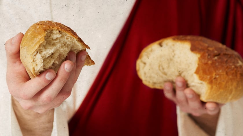 Pessoa de túnica clara e manto vermelho segura dois pedaços de pão partido.