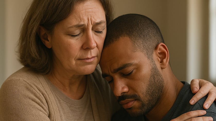 Mulher de meia-idade abraça um homem de barba curta, que apoia a cabeça nela.