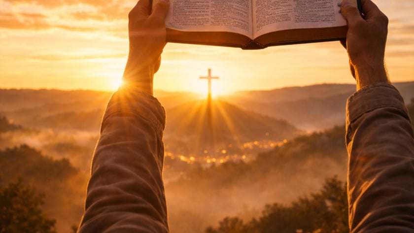 Duas mãos erguem uma Bíblia aberta diante de uma cruz sobre uma colina ao nascer do sol.