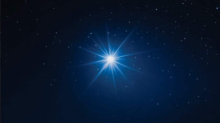 Estrela azul muito brilhante com raios longos, cercada por pequenas estrelas no céu escuro.