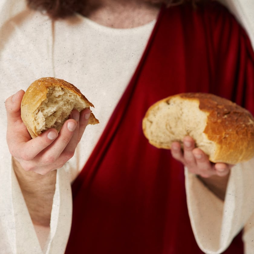Pessoa de túnica clara e manto vermelho segura dois pedaços de pão partido.
