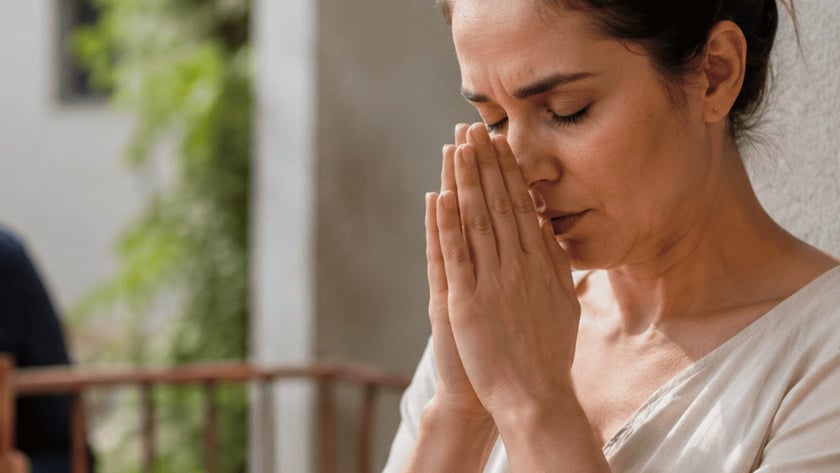 Mulher de olhos fechados e mãos unidas diante do rosto, em uma varanda.