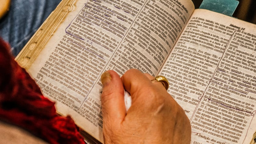 Mão de uma pessoa sobre uma Bíblia aberta e sublinhada em Mateus 14, em português.