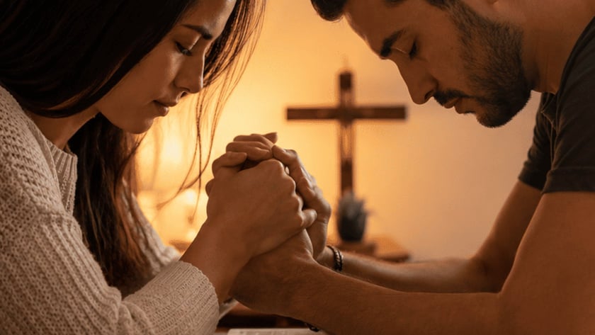 Mulher e homem de cabeça baixa, com as mãos unidas sobre uma Bíblia aberta, diante de uma cruz.