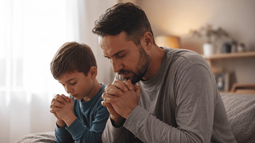 Homem e menino de mãos postas e olhos fechados, rezando lado a lado em um quarto.