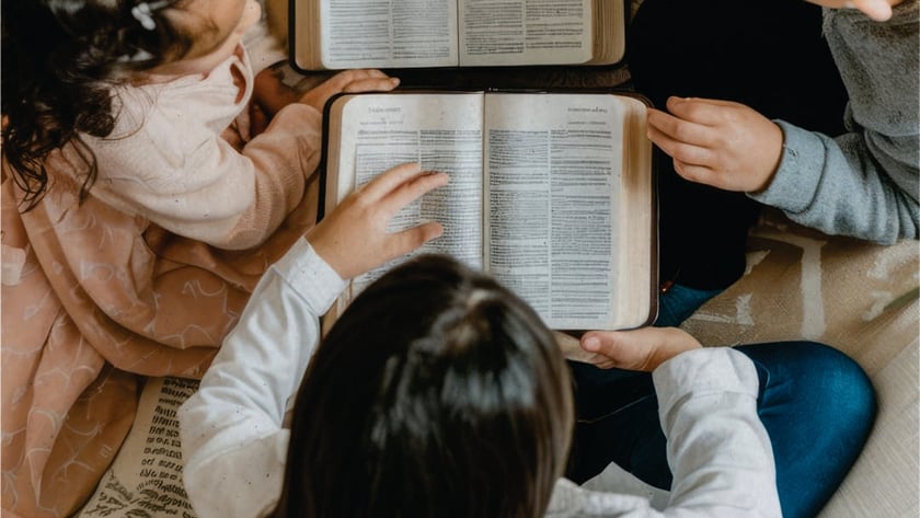 Crianças e adultos sentados em círculo no chão, lendo duas Bíblias abertas.