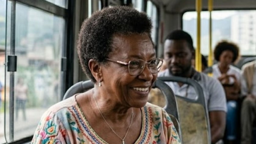 Idosa sorridente de óculos, com um livro no colo, sentada num ônibus ao lado de uma criança.