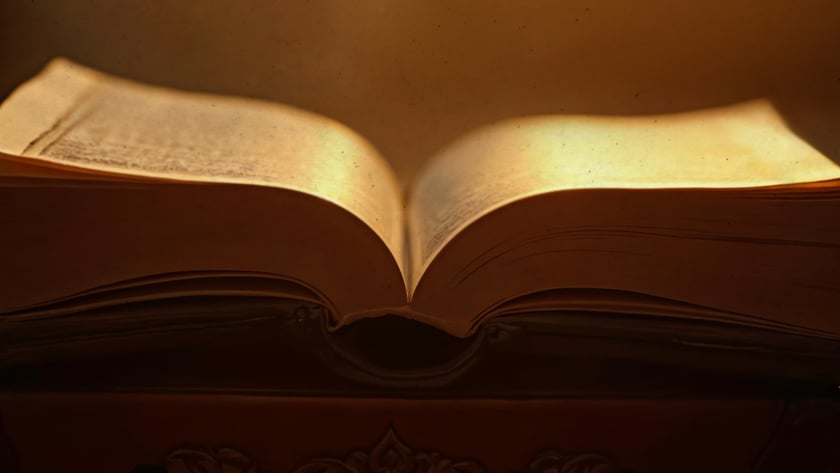 Livro antigo aberto sobre um móvel de madeira entalhada, com páginas amareladas.