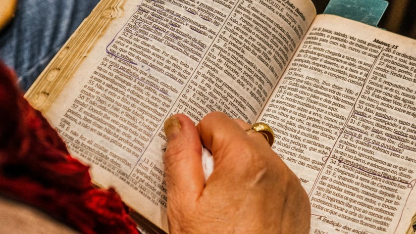 Mão de uma pessoa sobre uma Bíblia aberta e sublinhada em Mateus 14, em português.