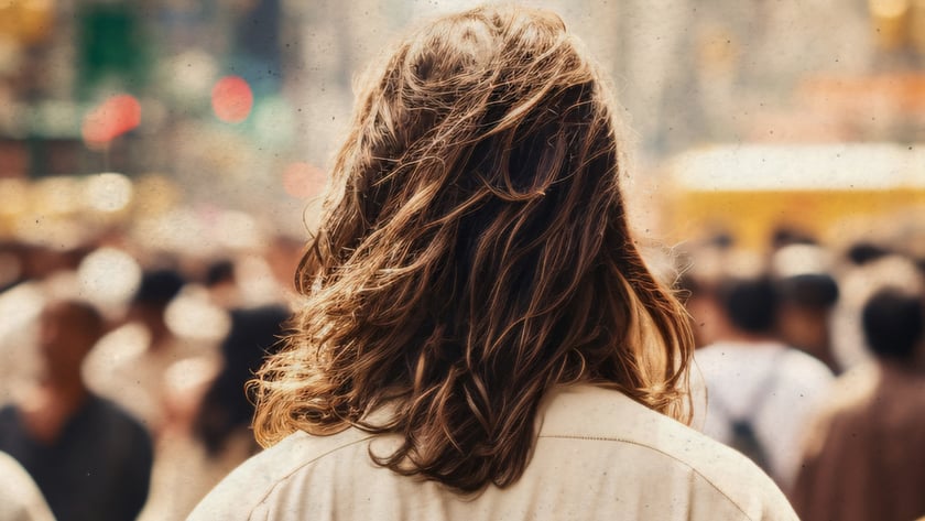 Pessoa de costas, com cabelo castanho ondulado e camisa clara, em meio a uma multidão