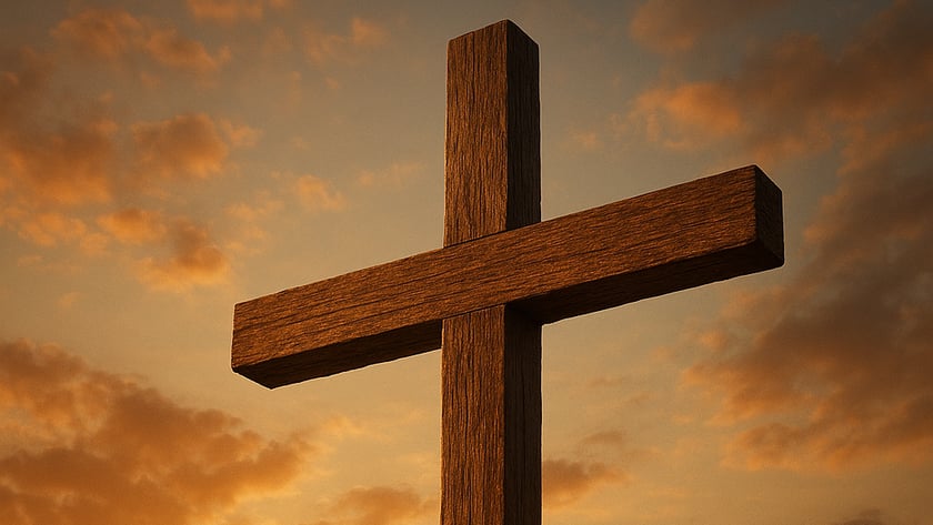 Cruz de madeira rústica contra o céu alaranjado com nuvens e o sol baixo.