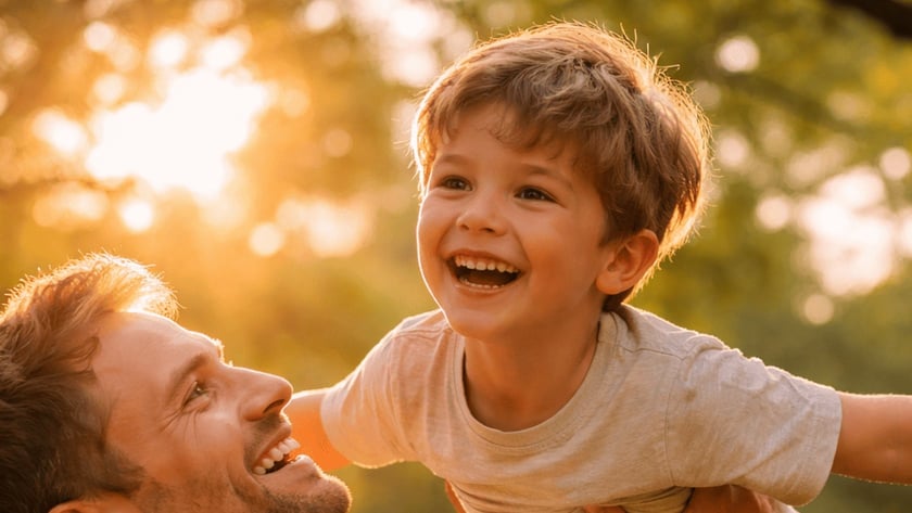Homem sorridente levanta um menino com os braços abertos, ao ar livre.
