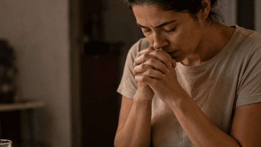 Mulher de olhos fechados e mãos juntas diante de pão, arroz e copo d'água.