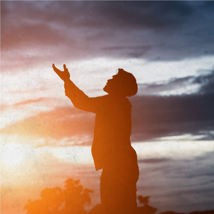 Silhueta de homem com o braço erguido e o rosto voltado para o céu ao entardecer.