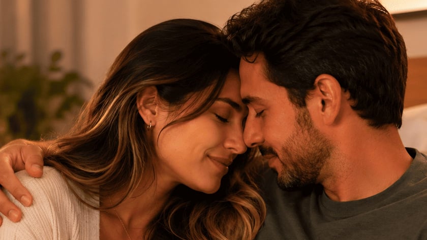 Casal sentado no sofá, de testas encostadas e mãos entrelaçadas, em ambiente aconchegante.