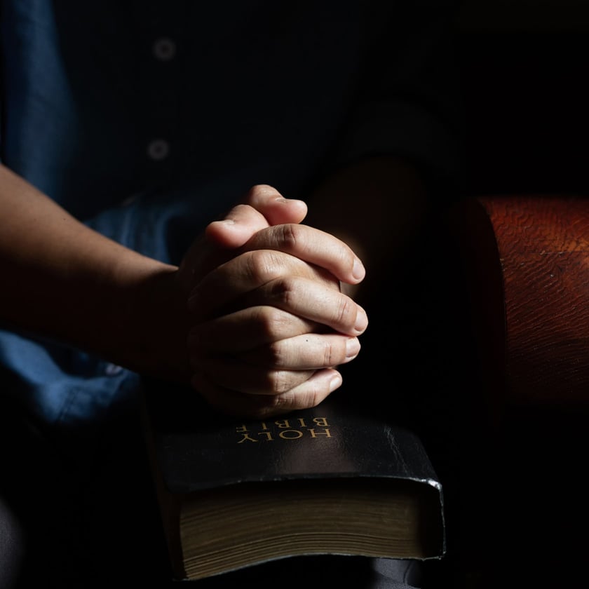 Mãos entrelaçadas sobre uma Bíblia preta fechada, com texto dourado "HOLY BIBLE".