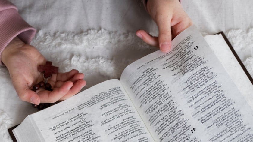 Mãos segurando um terço de madeira e virando a página de uma Bíblia aberta em "Salmos 45".
