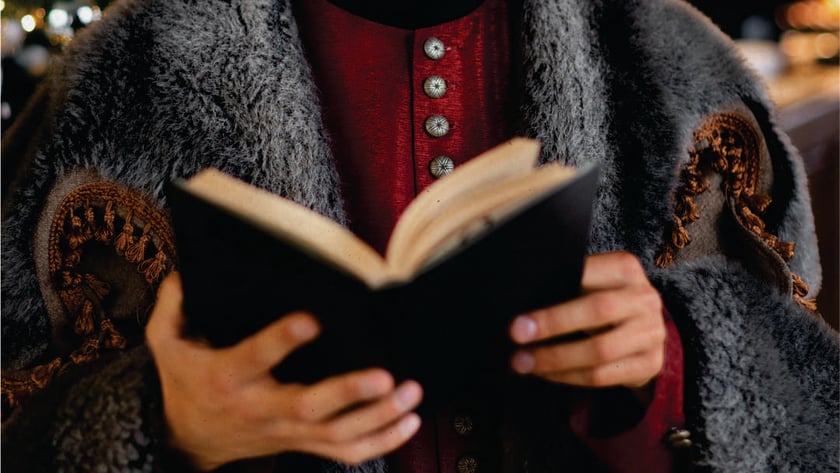 Pessoa com casaco vermelho e manto de pelo cinza lê um livro aberto.