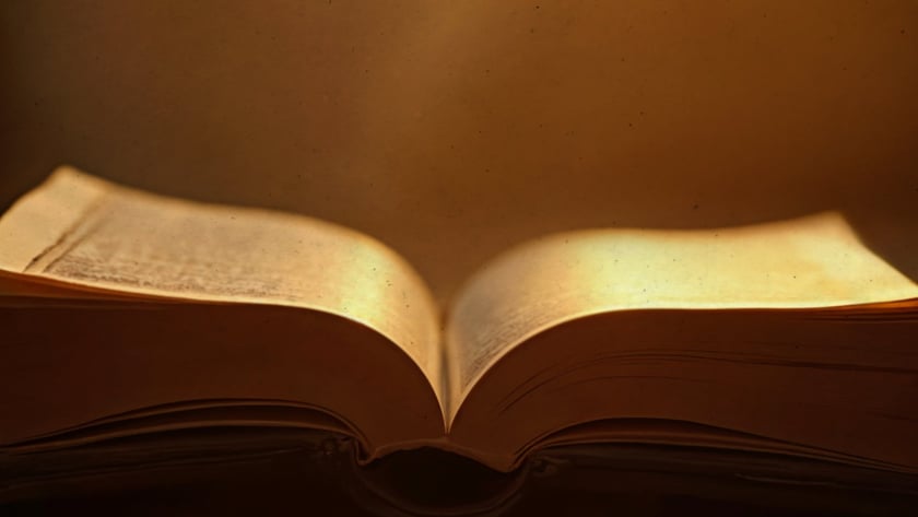 Livro antigo aberto sobre um móvel de madeira entalhada, com páginas amareladas.