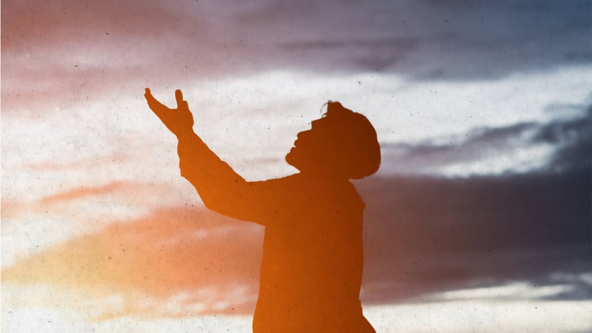 Silhueta de homem com o braço erguido e o rosto voltado para o céu ao entardecer.