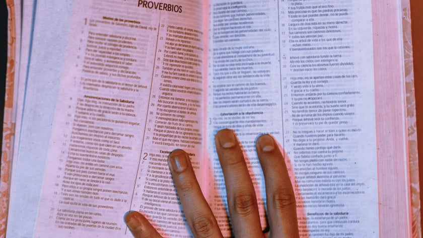 Mão espalmada sobre Bíblia aberta em espanhol, na página de "PROVERBIOS".