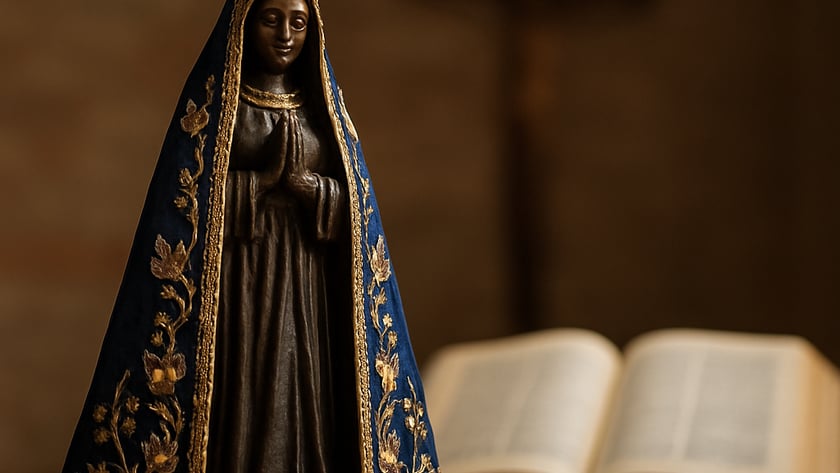 Estatueta de santa com coroa dourada e manto azul bordado, diante de uma Bíblia aberta.