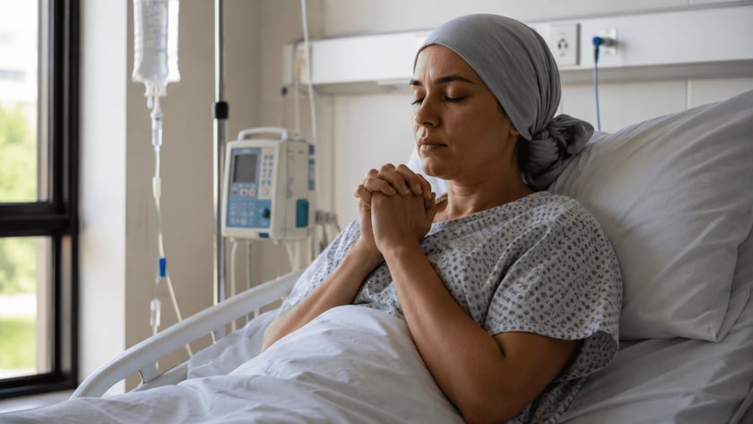 Mulher deitada em cama de hospital, de mãos juntas e olhos fechados, ao lado de soro.