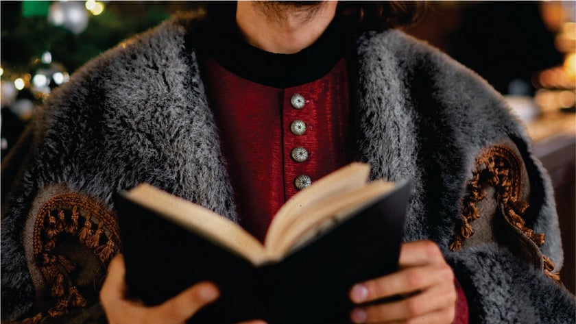 Pessoa com casaco vermelho e manto de pelo cinza lê um livro aberto.