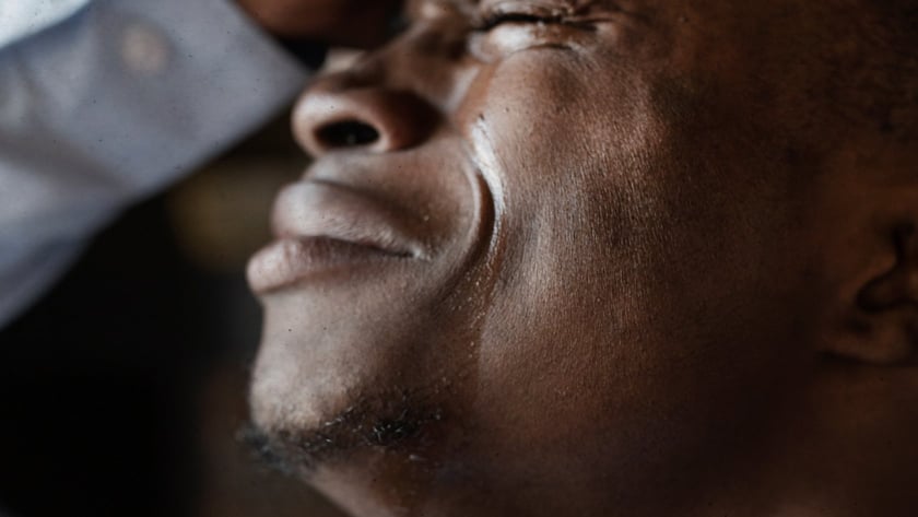 Homem de olhos fechados, com a mão na testa e lágrimas escorrendo pelo rosto.