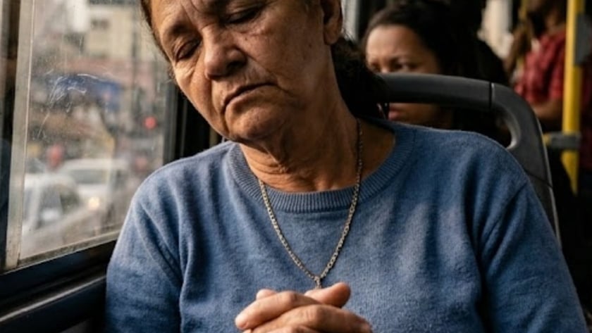 Mulher idosa de suéter azul, de olhos fechados, encosta a cabeça na janela do ônibus.