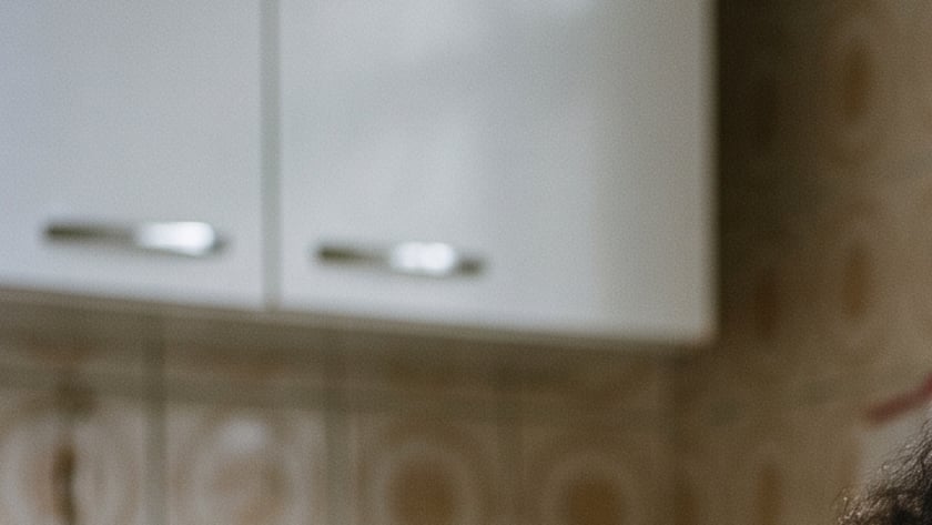 Mulher de olhos fechados com as mãos sobre uma Bíblia, à mesa da cozinha.