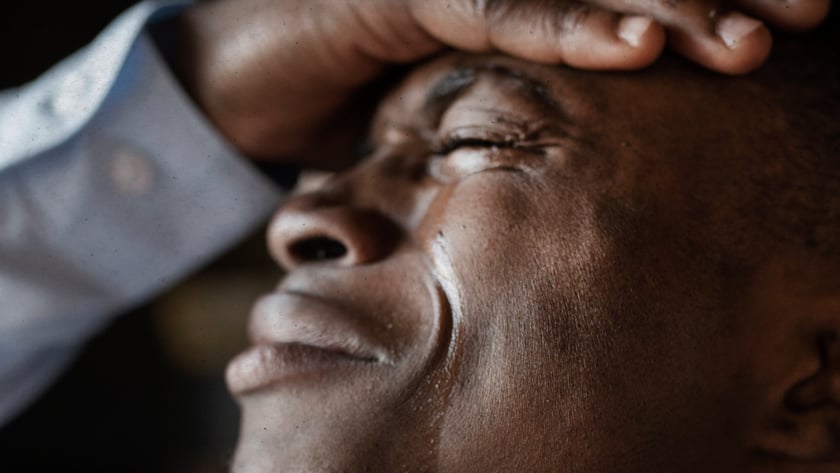 Homem de olhos fechados, com a mão na testa e lágrimas escorrendo pelo rosto.