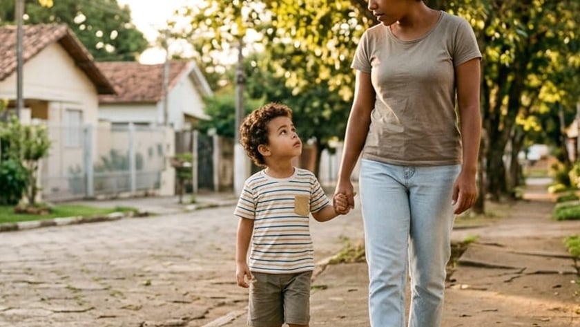 Mulher e menino de mãos dadas caminhando por uma calçada em rua de paralelepípedos.