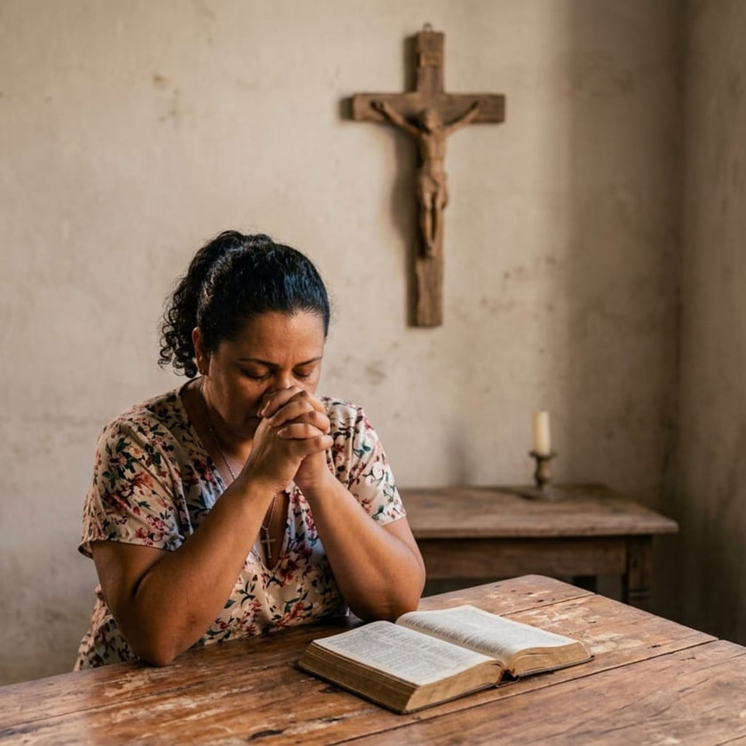 Mulher de olhos fechados e mãos juntas reza diante de uma Bíblia aberta, com crucifixo na parede.