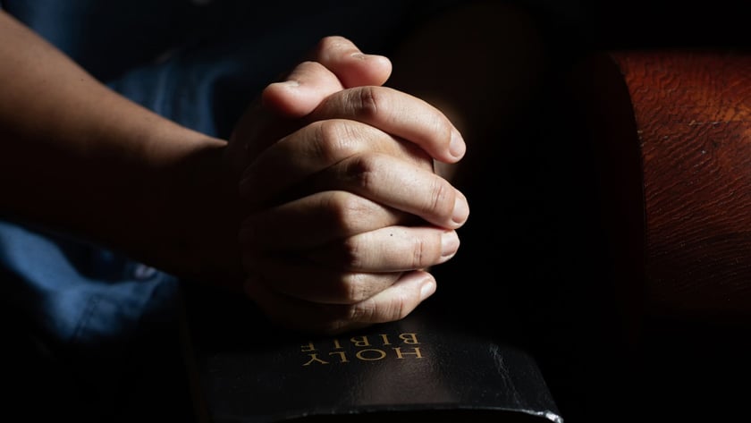Mãos entrelaçadas sobre uma Bíblia preta fechada, com texto dourado "HOLY BIBLE".