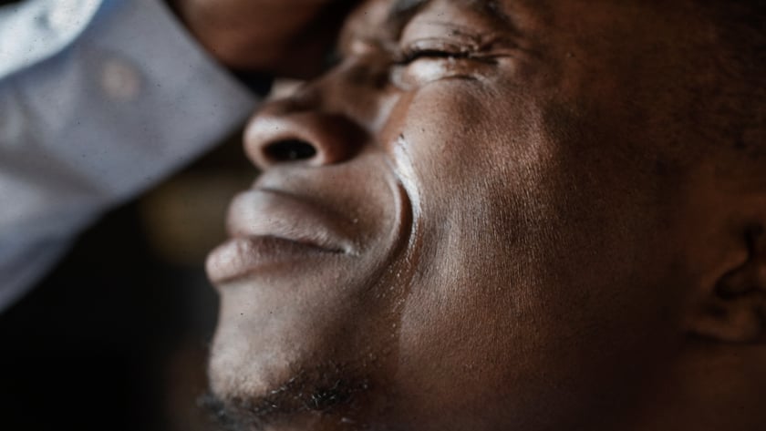 Homem de olhos fechados, com lágrimas no rosto, apoia a mão na testa.