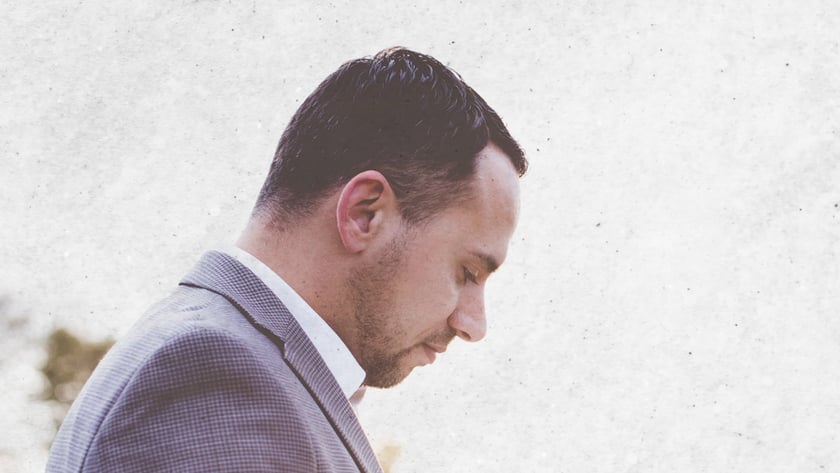 Homem de blazer cinza olha para um livro aberto em suas mãos, ao ar livre.