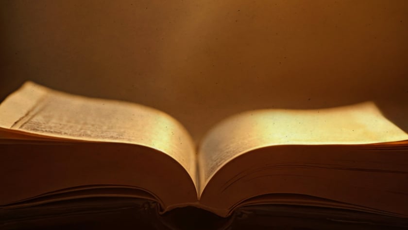 Livro antigo aberto sobre um móvel de madeira entalhada, com páginas amareladas.