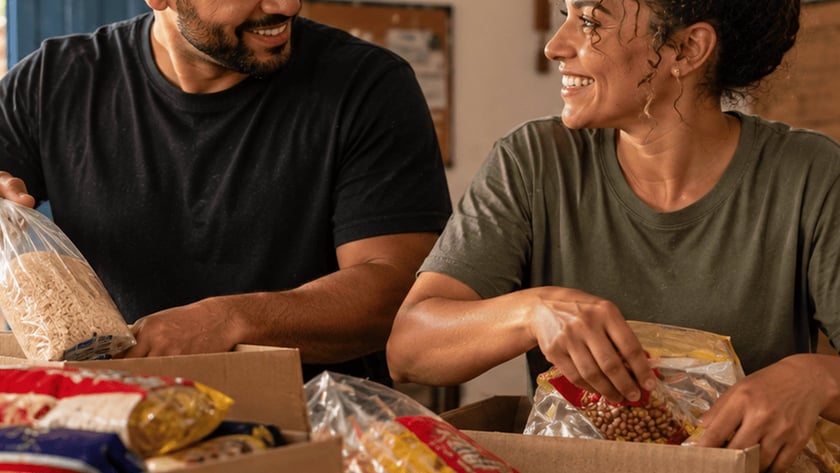 Dois voluntários sorridentes organizam alimentos em caixas de papelão