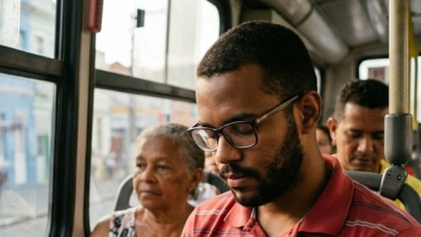 Homem de óculos segura uma Bíblia com cruz dentro de um ônibus, ao lado de uma senhora.