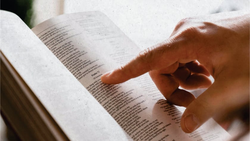 Mão apontando com o dedo indicador para um trecho de uma Bíblia aberta: "Psalm 72".