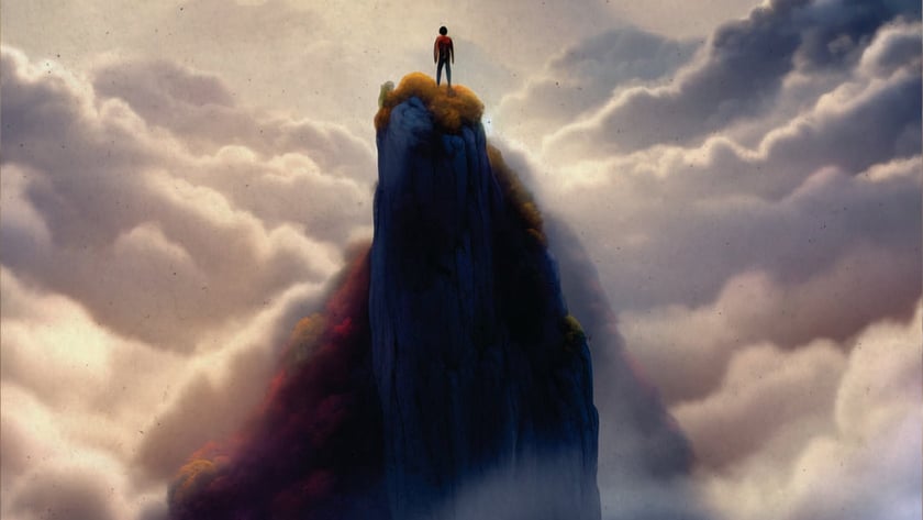 Pessoa de pé no topo de um pico rochoso, acima de nuvens e montanhas.